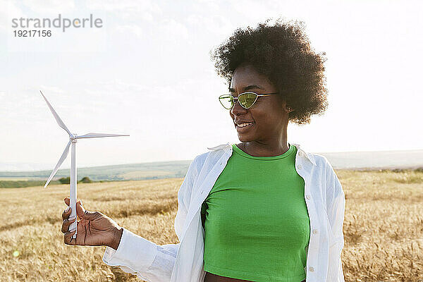 Smiling woman holding wind turbine in field