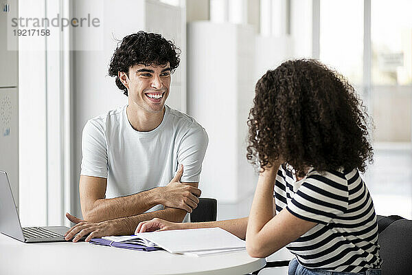 Lächelnde Studenten kommunizieren am Tisch in der Universität