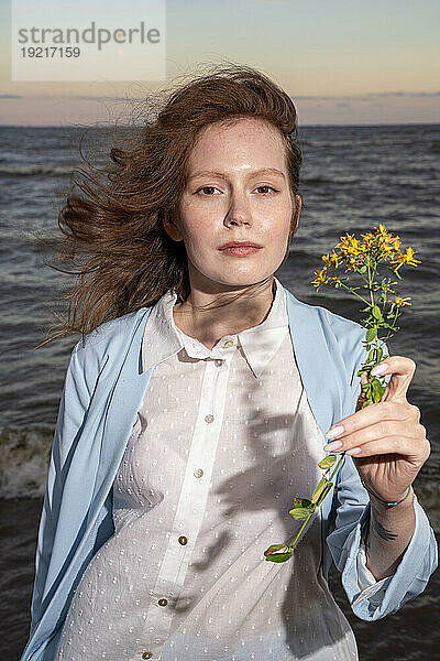 Junge Frau hält gelbe Blumen am Strand