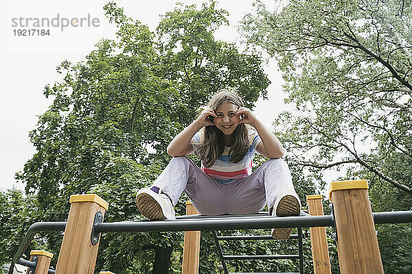 Glückliches Mädchen sitzt im Klettergerüst auf dem Spielplatz