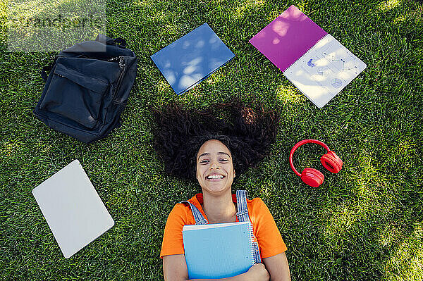 Lächelnder Student liegt mit Spiralnotizbüchern auf dem Gras auf dem Campus