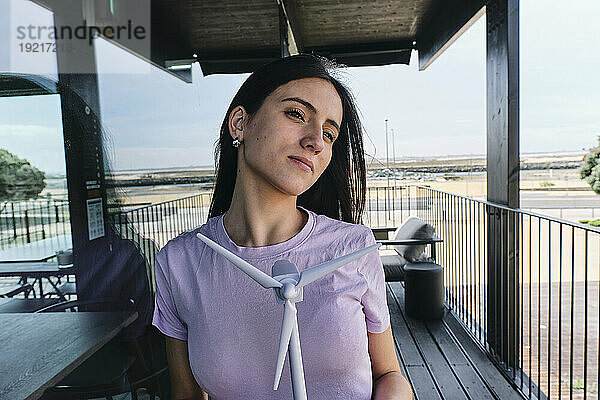 Portrait of beautiful brunette standing on balcony with model of wind turbine in hands