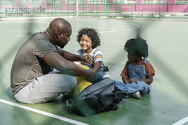 Vater sitzt mit Kindern auf dem Boden des Sportplatzes