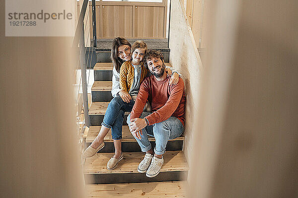 Smiling man sitting with woman and daughter on staircase at home