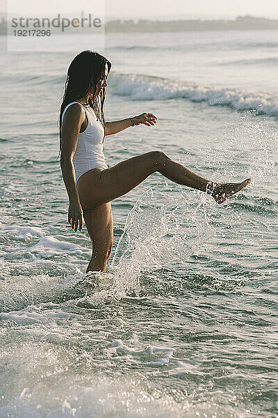 Verspielte Frau  die am Strand Wasser tritt