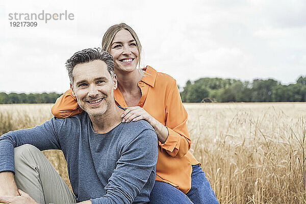 Lächelnde Frau sitzt mit Mann auf dem Feld