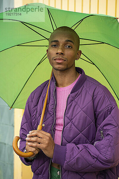Nicht-binäre Person mit grünem Regenschirm