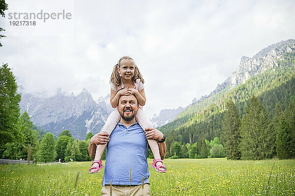 Glücklicher Mann trägt Tochter auf Schultern vor Bergen
