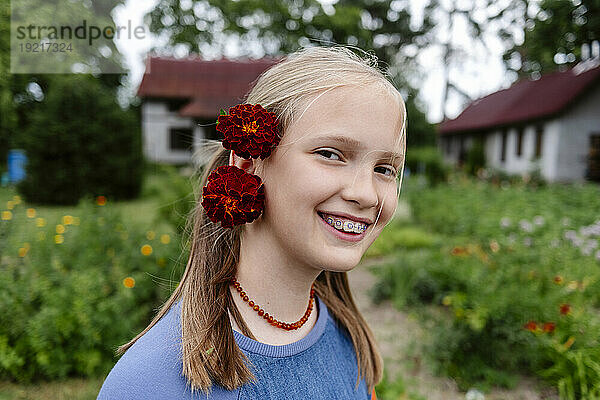 Lächelndes Mädchen mit Blumen auf dem Kopf im Garten
