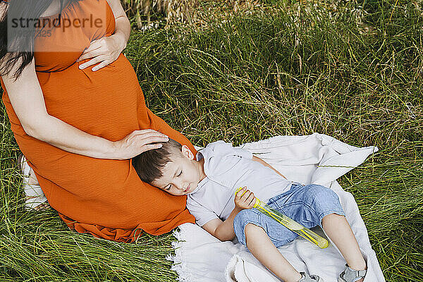 Pregnant mother stroking sleeping son on grass