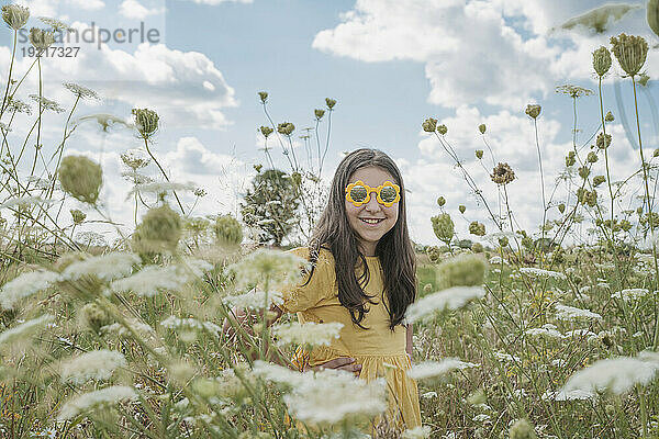 Lächelndes Mädchen mit Sonnenbrille inmitten von Blumen im Feld