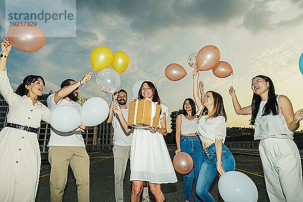 Fröhliche Freunde feiern den Geburtstag der Frau mit Luftballons und Geschenken unter bewölktem Himmel