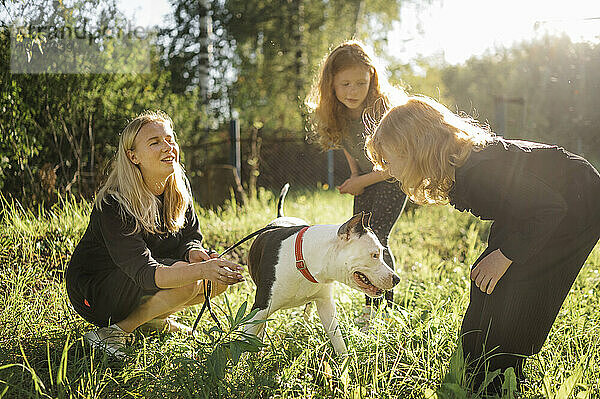 Mutter und Töchter spielen an einem sonnigen Tag mit Hund im Park