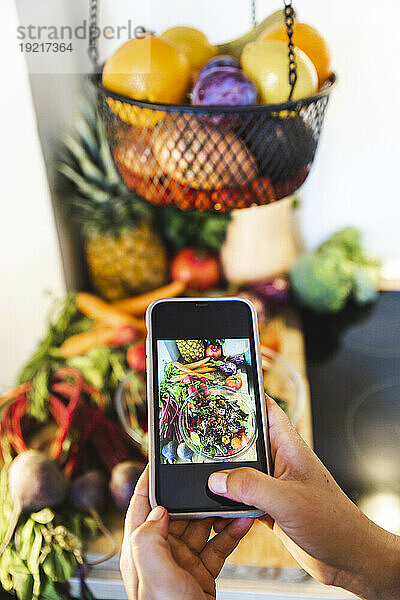 Hände einer Frau  die zu Hause in der Küche Gemüse und eine Schüssel Salat fotografiert