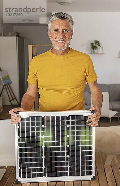 Lächelnder Ingenieur mit Solarpanel  der zu Hause steht