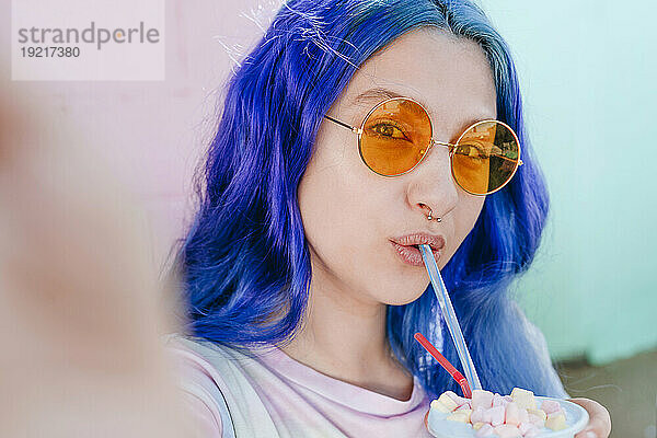 Hipster-Frau mit gefärbten blauen Haaren hält Getränk in der Hand und macht Selfie im Café