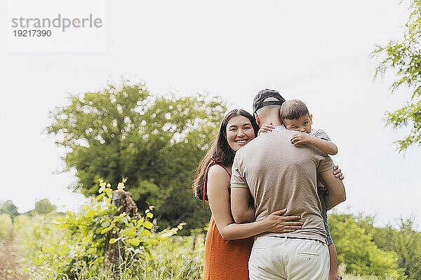 Lächelnde Frau umarmt Familie in der Nähe von Pflanzen