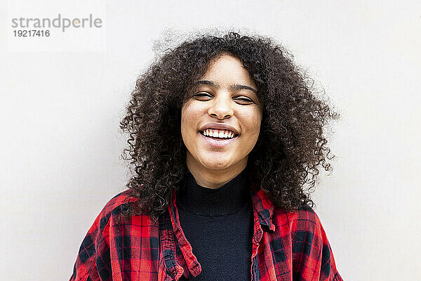Happy woman with curly hair in front of wall
