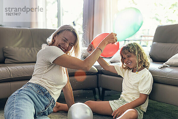 Glückliche Mutter und Tochter spielen mit Luftballons im Wohnzimmer