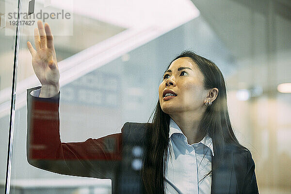 Selbstbewusste Geschäftsfrau berührt Glaswand am Arbeitsplatz