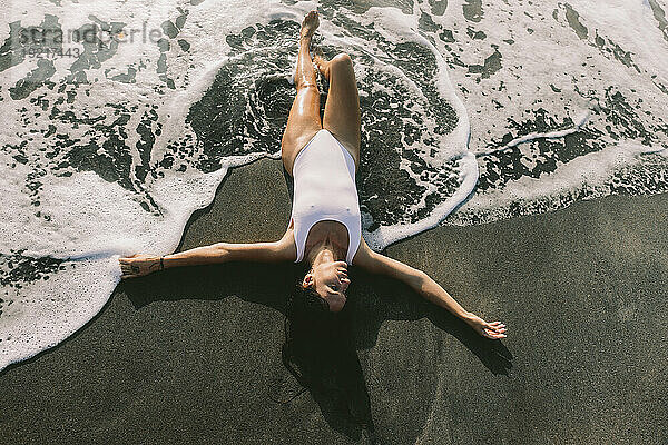 Sorglose Frau liegt auf schwarzem Sand am Strand