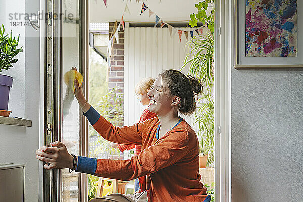 Smiling teenage girl cleaning door with sister in background at home