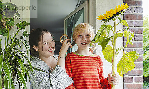 Happy girl with big sunflower standing by sister on balcony