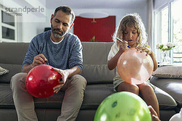 Tochter und Vater zeichnen im Wohnzimmer Luftballons