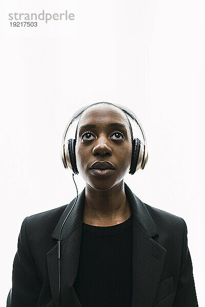 Nachdenkliche junge Frau mit Kopfhörern vor weißem Hintergrund