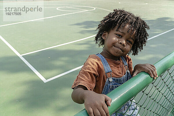 Smiling boy standing near fence on sports court