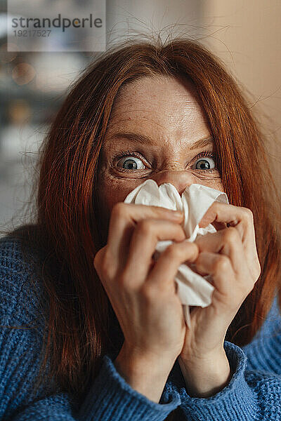 Rothaarige Frau putzt sich zu Hause auf Seidenpapier die Nase