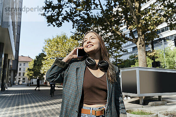 Lächelnde Frau  die an einem sonnigen Tag mit dem Smartphone spricht