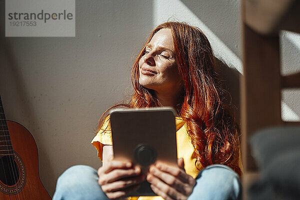 Smiling redhead woman sitting with eyes closed near wall