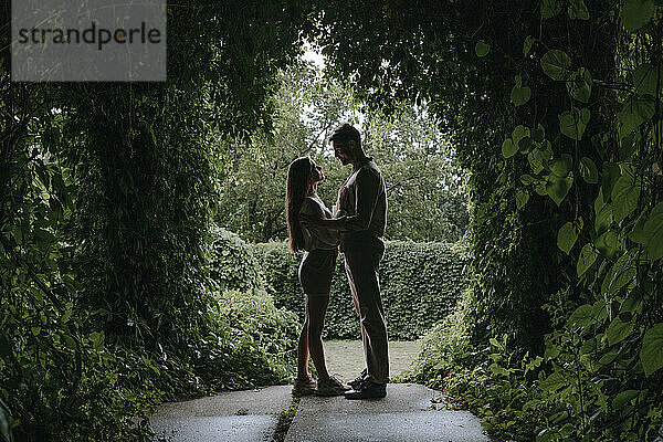 Junges Paar steht unter Pflanzenbogen im Garten