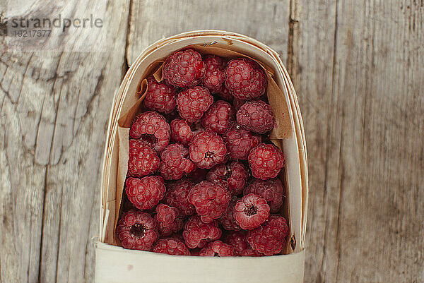 Wooden box with raspberries on table