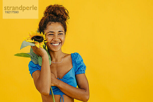 Glückliche junge Frau hält Sonnenblume vor gelbem Hintergrund
