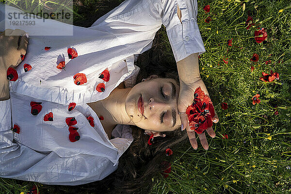 Lächelnde junge Frau entspannt sich im Gras mit Mohnblumen