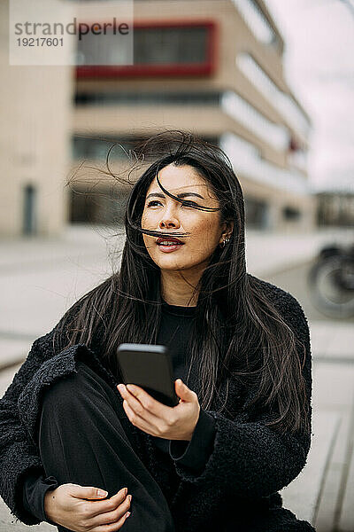 Geschäftsfrau mit Smartphone sitzt vor Bürogebäude