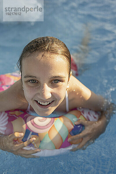 Lächelndes Mädchen schwimmt mit aufblasbarem Schwimmring im Schwimmbad