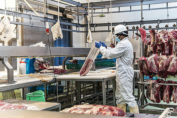 Junger Metzger verpackt rohes Fleisch im Schlachthof