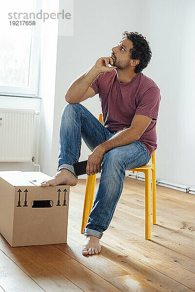 Nachdenklicher Mann sitzt zu Hause auf einem Stuhl neben einer Kiste