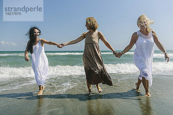 Freunde halten Händchen und gehen gemeinsam am Strand spazieren