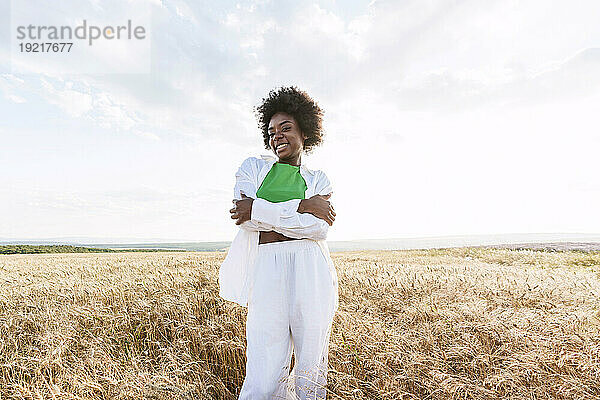 Happy young woman hugging self standing in field