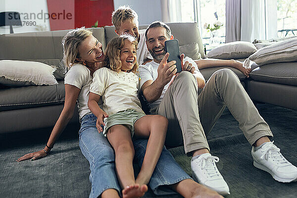 Lächelnder Mann macht ein Selfie mit der Familie auf dem Smartphone im Wohnzimmer