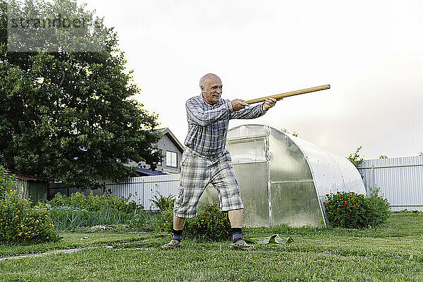 Älterer Mann spielt mit Holzstab im Garten
