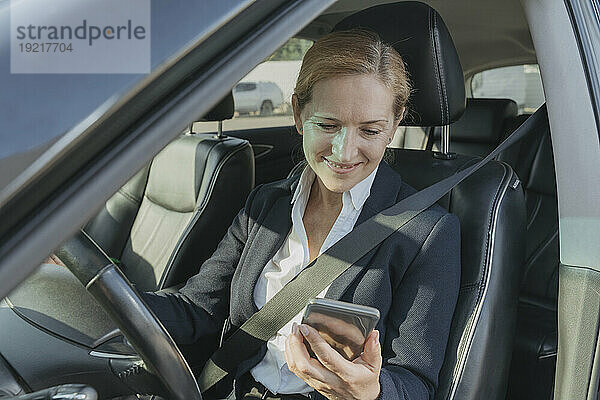 Lächelnde Geschäftsfrau benutzt Mobiltelefon im Auto