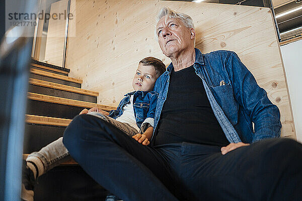 Grandson and grandfather sitting on staircase at home