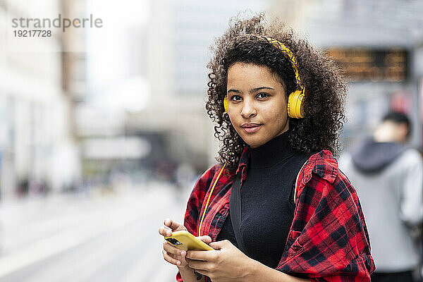 Lächelnde Frau  die in der Stadt Musik über Kopfhörer hört