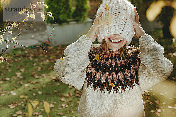 Smiling girl covering face with knit hat in garden