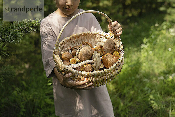 Mädchen hält Korb voller Pilze im Wald